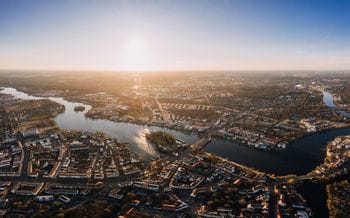 Luftaufnahme von Köpenick bei Sonnenuntergang, die den Stadtteil mit seinen Wasserwegen, der dichten Wohnbebauung und der charakteristischen Flusslandschaft zeigt. Die warme Abendbeleuchtung hebt die Struktur der Stadt und die sich schlängelnden Gewässer hervor.