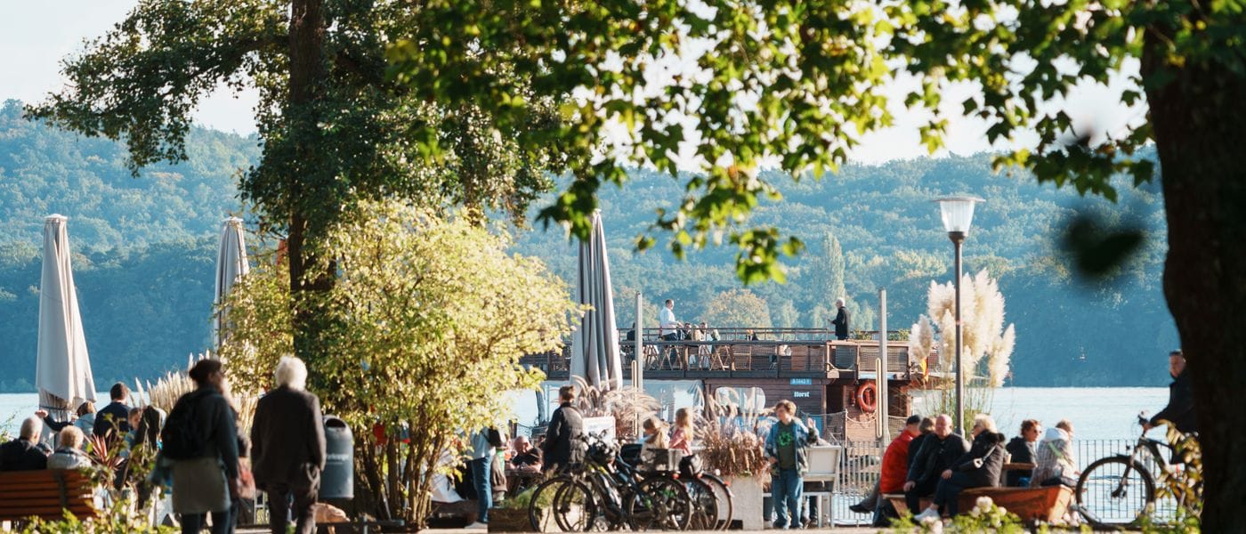Der Buddybär von Treptow-Köpenick vor der Touristinformation am Schlossplatz. Eine bunte Bärenskulptur in Matrosenuniform steht im Schnee vor dem Touristeninformationszentrum mit roten Fensterrahmen. Die Skulptur trägt eine blaue Uniform mit rotem Bauch und hat die Arme nach oben gestreckt, während Schnee fällt.